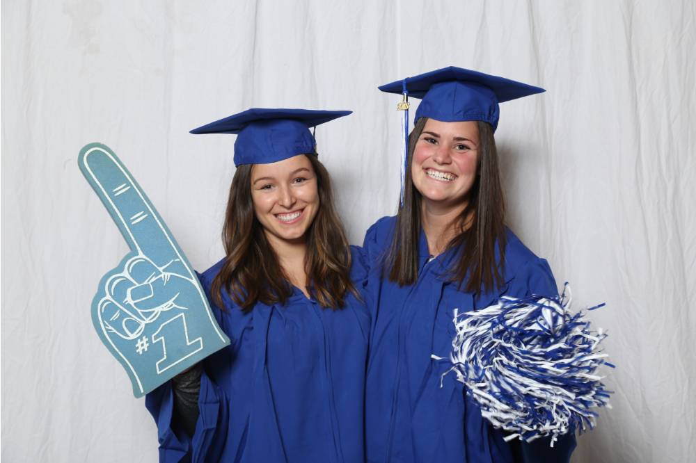 Two graduates pose together with cap and gowns on at GradFest